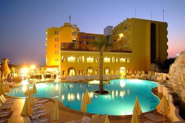 Esra Palace Hotel'in gece aydınlatılmış sarı binası ve havuzu