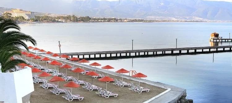 Vista Hill'in plajı; kırmızı şemsiyeler ve iskele, sisli dağ önünde