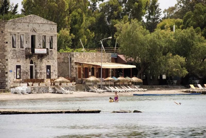 Bodrum yarımadasında sığ bir koy, kıyıdaki eski taş yapı ve hasır şemsiyeli plaj