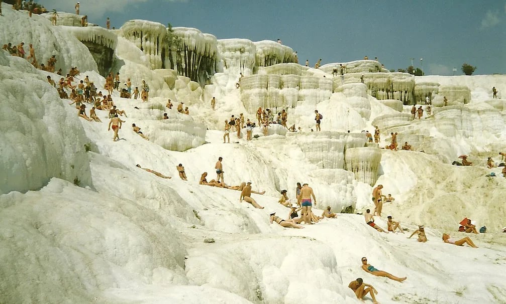 Pamukkale travertenlerinde güneşlenen kalabalık; basamaklı beyaz kalsiyum terasları ve sarkıt biçimli oluşumlar