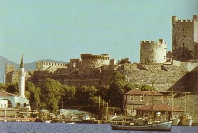 Bodrum Kalesi'nin eski bir fotoğrafı; önde kıyı ve yelkenli tekne