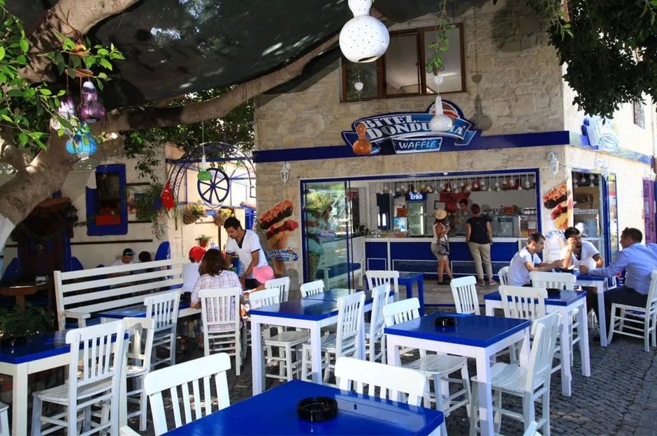 Bodrum'da beyaz-mavi masalarıyla asma altında bir sokak lokantası