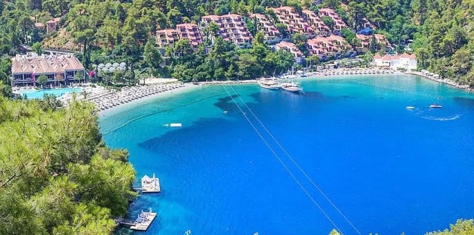 Orman çevrili koyda plaj ve yamaca kurulu tatil köyü, havadan