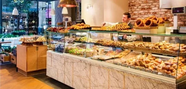 Pastane vitrini; tezgâhın arkasında börek dizen görevli