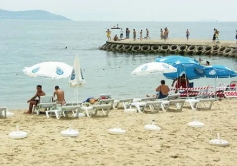 Caddebostan plajında şemsiyeler, şezlonglar ve taş iskelede yüzenler