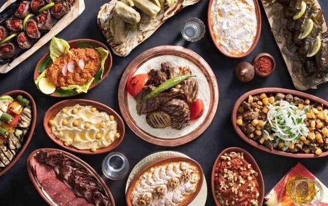 Ahşap sofrada yöresel kebap, meze ve tatlı tabakları, üstten