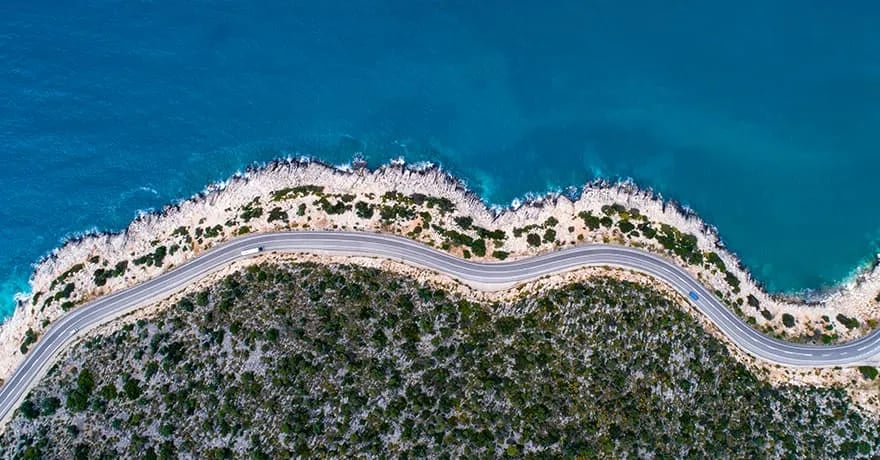Kıyı boyunca kıvrılan sahil yolu ve turkuaz deniz, havadan