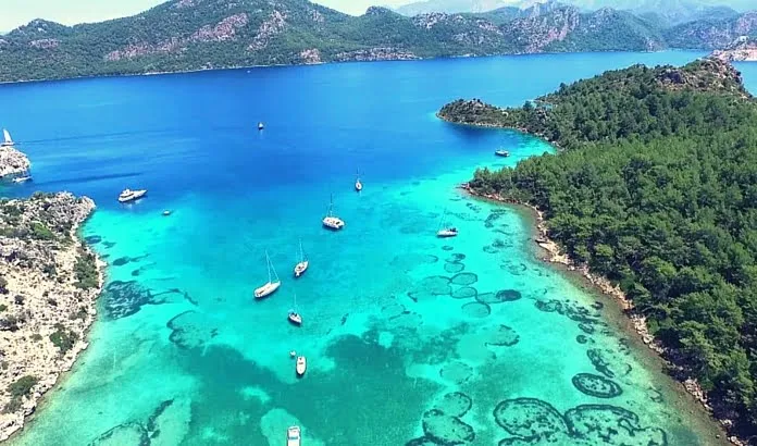 Hisarönü körfezi: turkuaz sığlıkta demirli yelkenliler ve çam kaplı burunlar