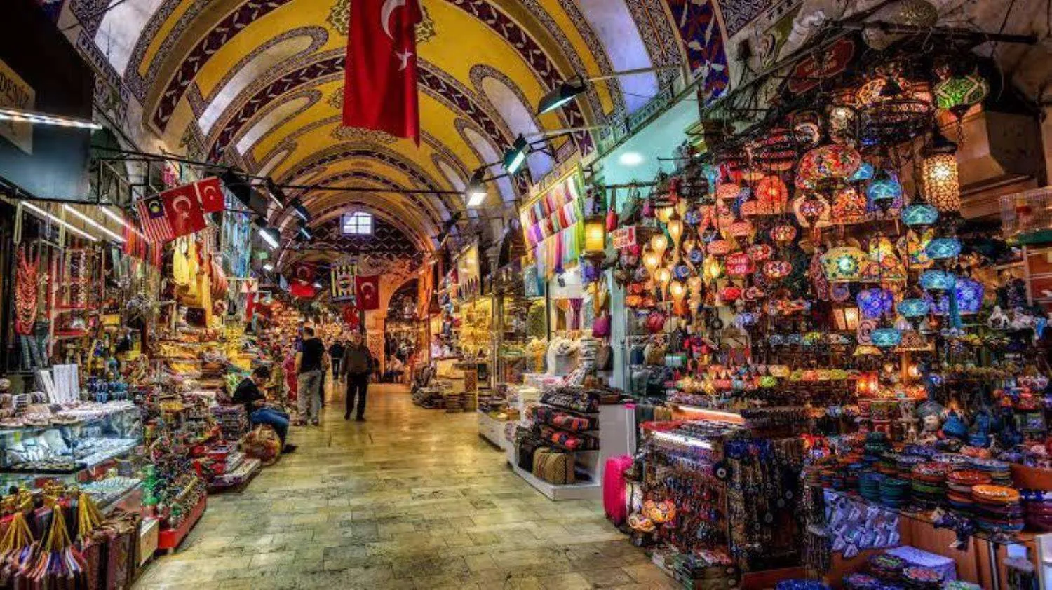 Bayraklarla süslü, boyalı tonozlu tarihî kapalı çarşı; fener ve hediyelik dükkânları