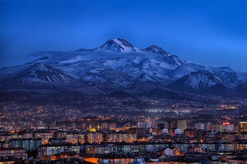 Akşam mavisinde karla kaplı Erciyes Dağı ve eteğinde Kayseri şehrinin ışıkları