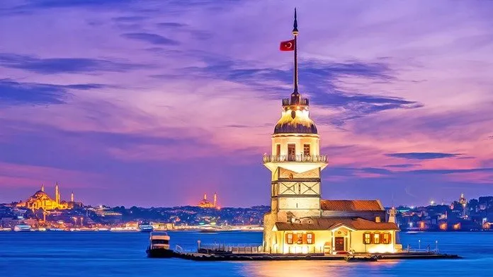 Alacakaranlıkta ışıklandırılmış Kız Kulesi; arkada tarihî yarımada silueti