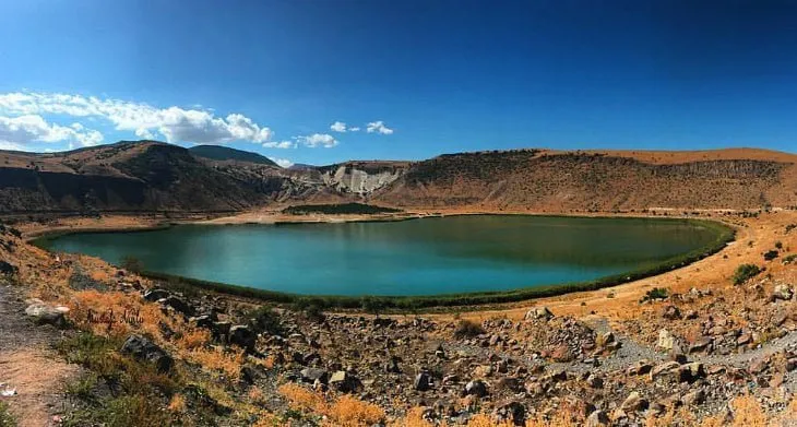 Narlıgöl krater gölünün yaz ortasında panoramik görünümü; turkuaz su ve çıplak, kavruk krater kenarı