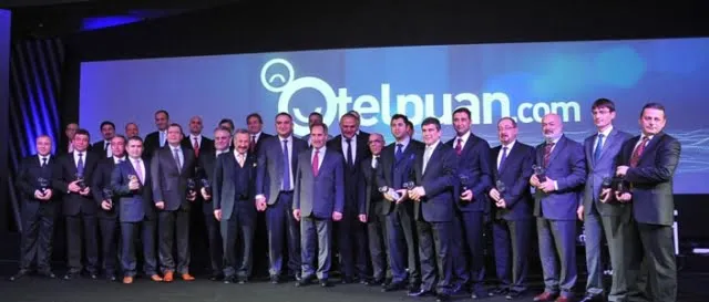 Ödül töreninde sahnede toplu fotoğraf veren takım elbiseli yöneticiler; arkada Otelpuan.com ekranı