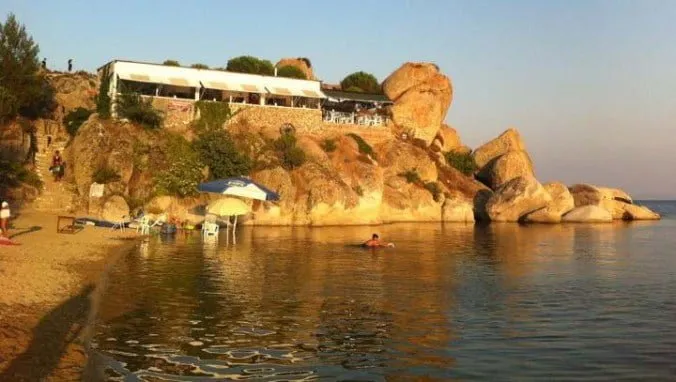 Kayalıkların üzerine kurulu restoran ve altındaki küçük plaj koyu, akşam ışığında