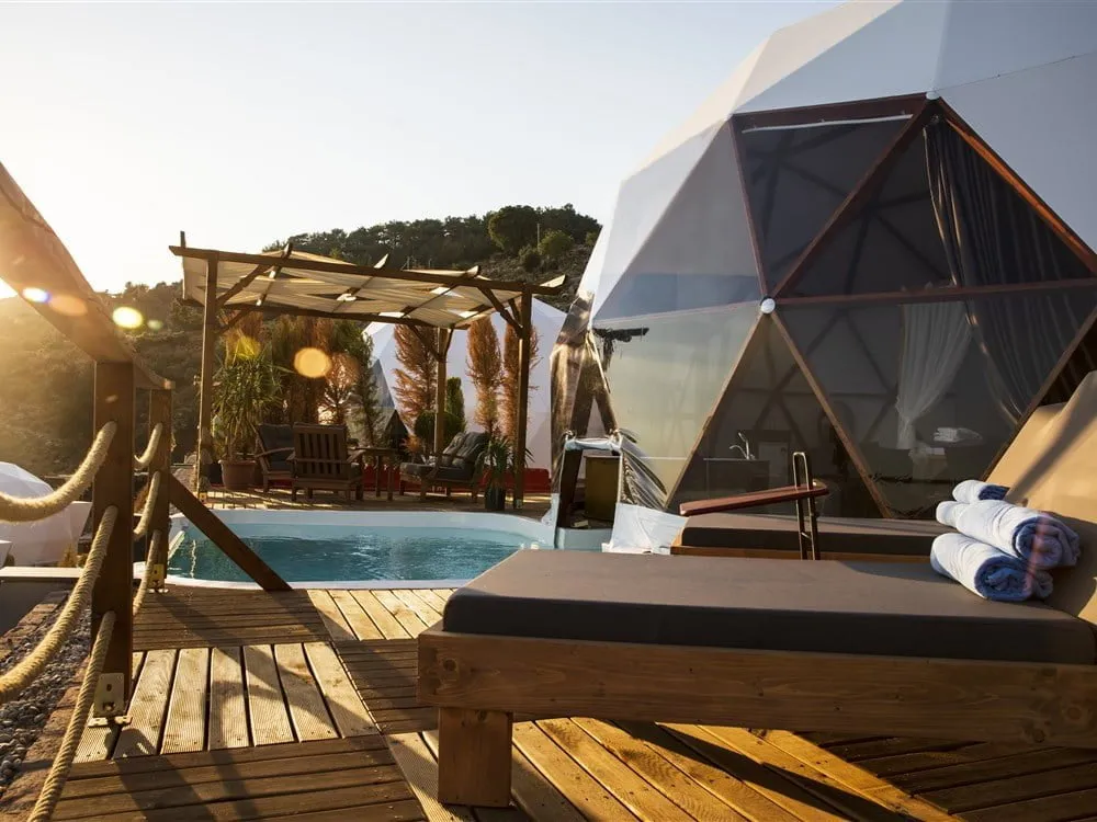 Gün batımında ahşap teraslı dome çadır; önünde küçük havuz ve pergola