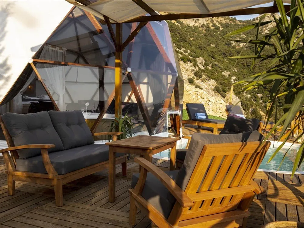 Pergola altında koltuklu oturma köşesi; arkada dome çadır ve yamaç