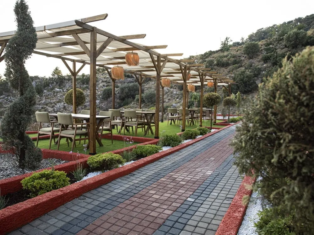 Taş yürüyüş yolu boyunca pergolalar altında restoran masaları