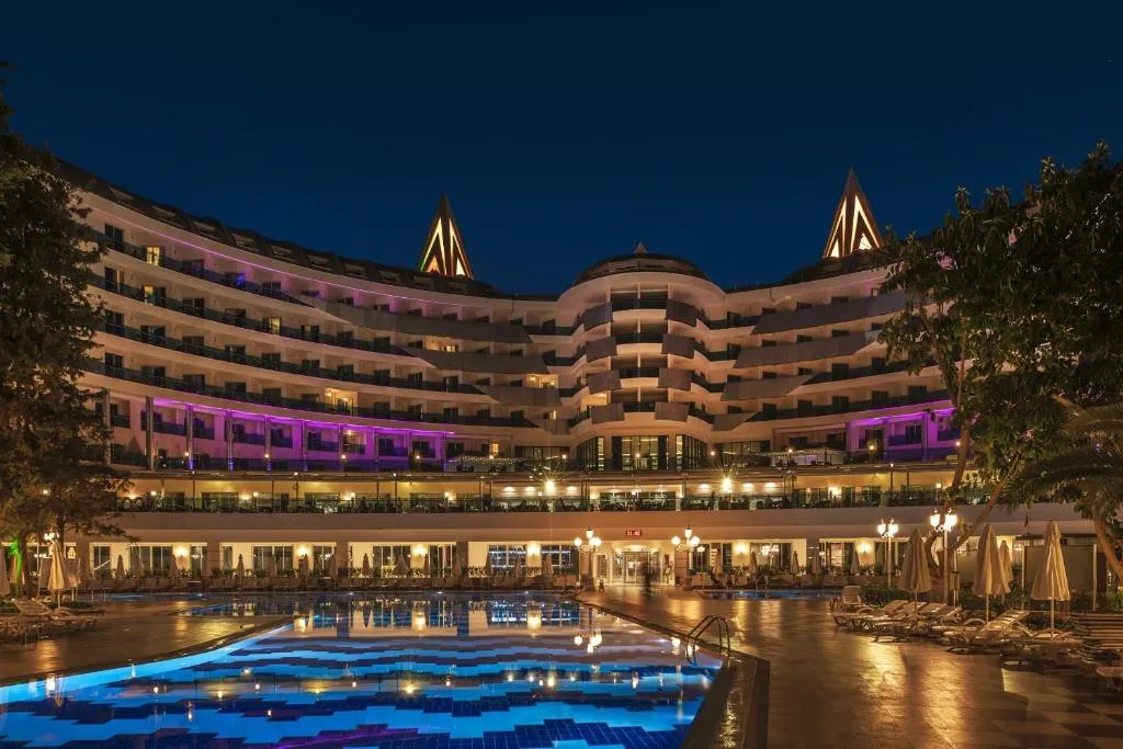 Gece aydınlatmalı yarım daire otel bloğu ve önündeki havuz